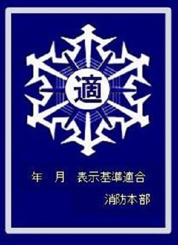 紺地に白色で、中央に「適」と書かれた徽章のデザインと、「年月 表示基準適合 消防本部」と記載された防火対象物用の適合マーク
