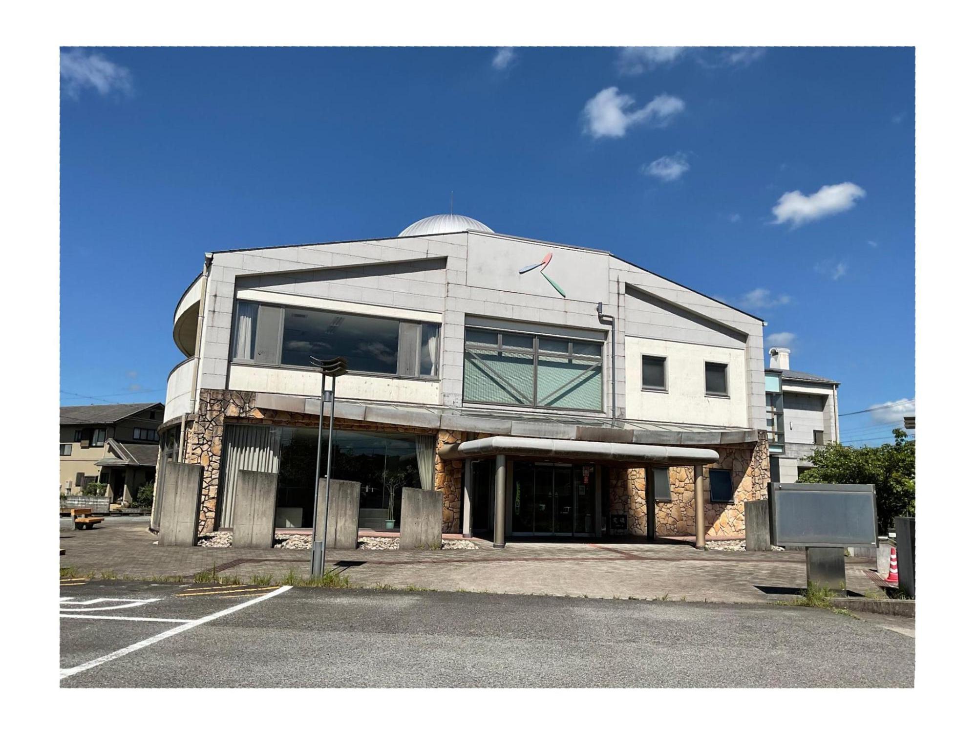 白とグレーの外壁の2階建てで、2階に大きな窓がある美祢来福センターの外観写真