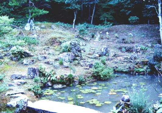 周りは森に囲まれ石がごつごつとした敷地の真ん中に池がある明林寺庭園の写真