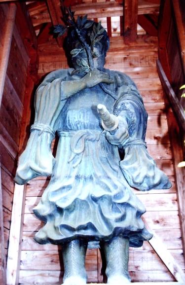 右手に榊の枝を持ち、その手を胸にあてており、左手には刀を持って立っている銅造猿田彦立像の写真