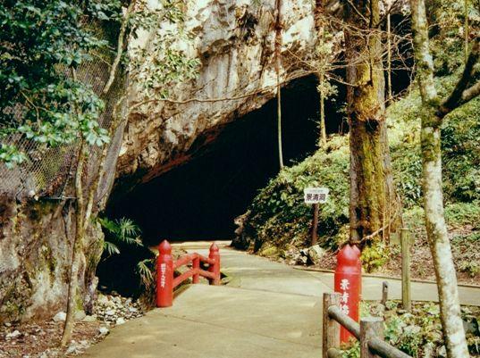 山の中に整地された歩道と赤い小さな橋があり奥に景清穴がある写真