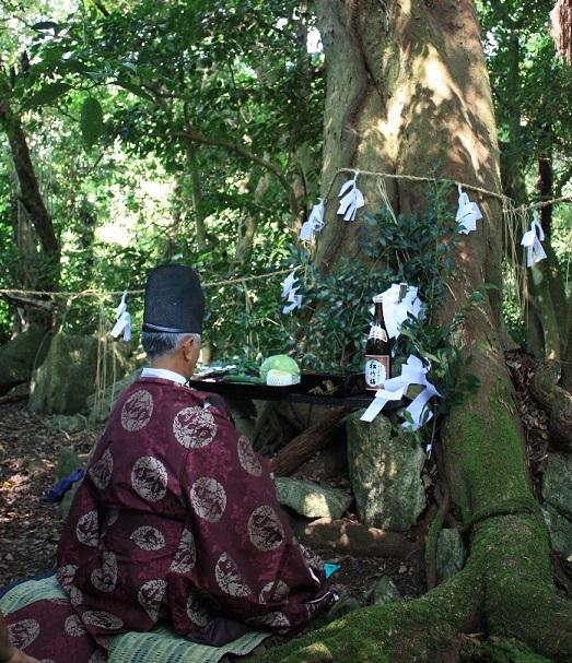江原の森の木にお供え物をし神主さんが前に座っている写真