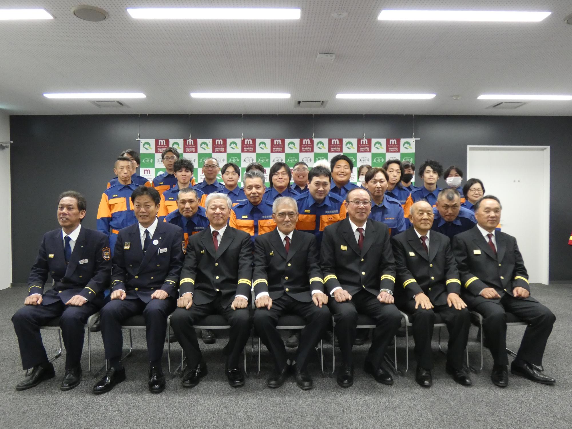 消防団長を中心に並ぶ幹部団員と新任団員の集合写真