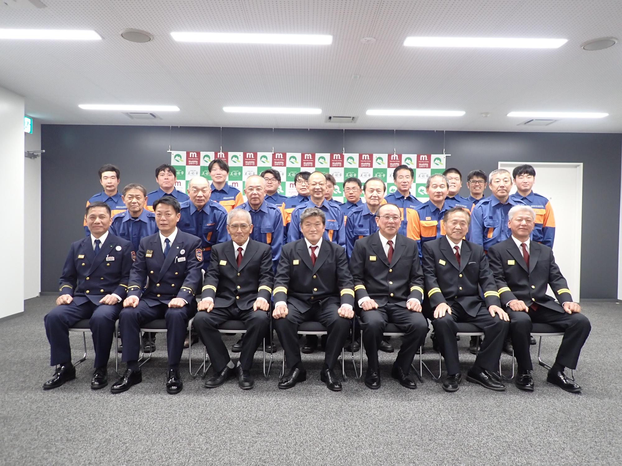 消防団長を中心に並ぶ幹部団員と新任団員の集合写真