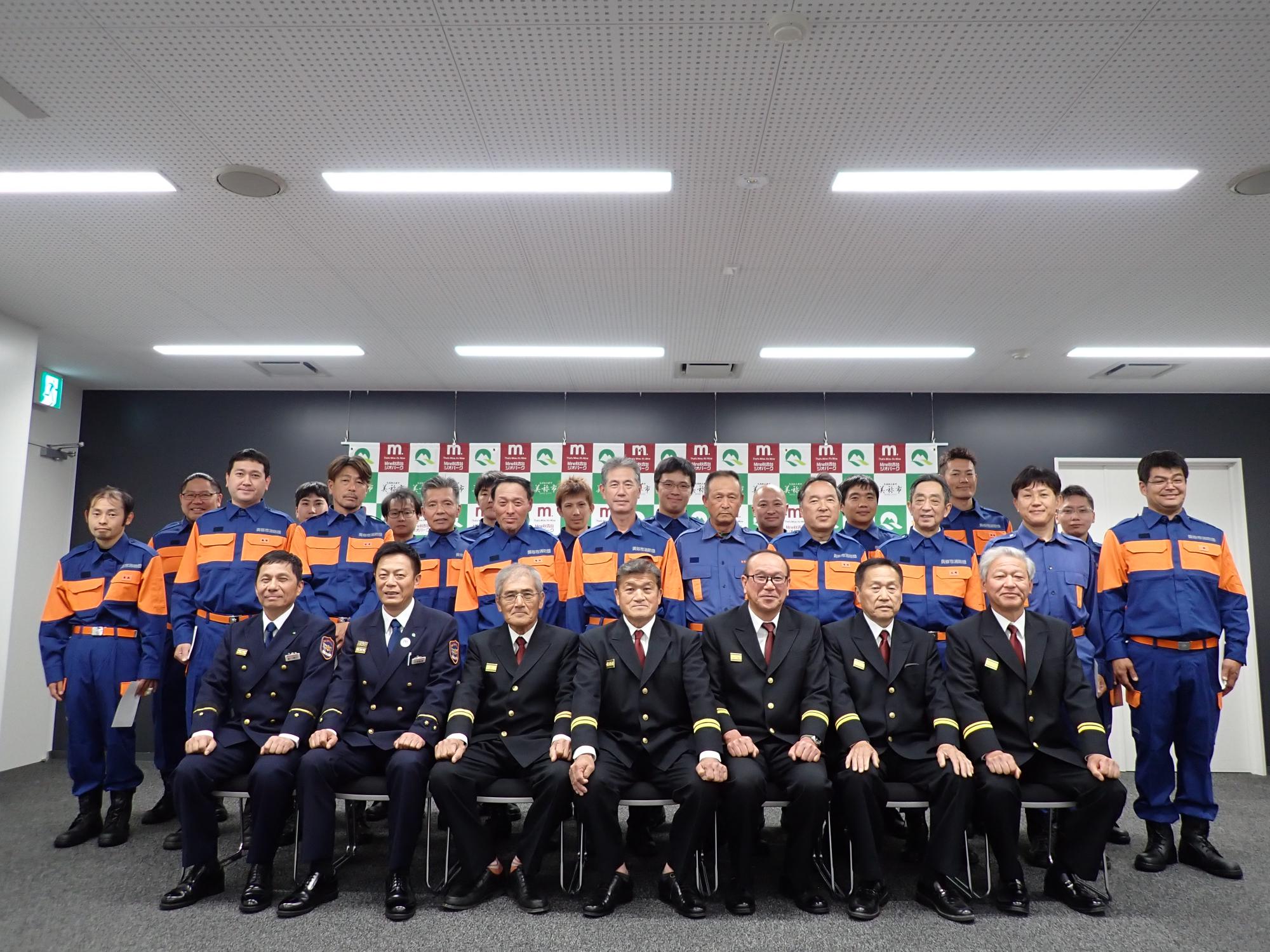 消防団長を中心に並ぶ幹部団員と新任団員の集合写真