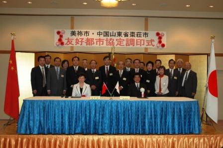 右側に日本国旗、左側に中国国旗が置かれた舞台上で撮影した美祢市長と棗荘市副市長、調印式参加者の記念写真
