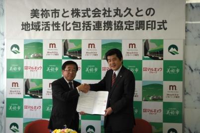 美祢市と株式会社丸久との地域活性化包括連携協定調印式で、互いに握手する丸久の関係者の方と市長の写真