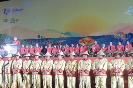 台湾ランタンフェスティバルの点灯式の様子で笠を被り黄色の衣装を着ている人が前列に、赤い上着を着ている人たちが後列に並んでいる写真