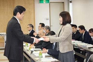 村田市長から委嘱状を手渡されている女性と長机に座って資料を見ている参加者の写真