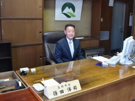 大きな木の机の前に座って微笑む美祢市長の写真